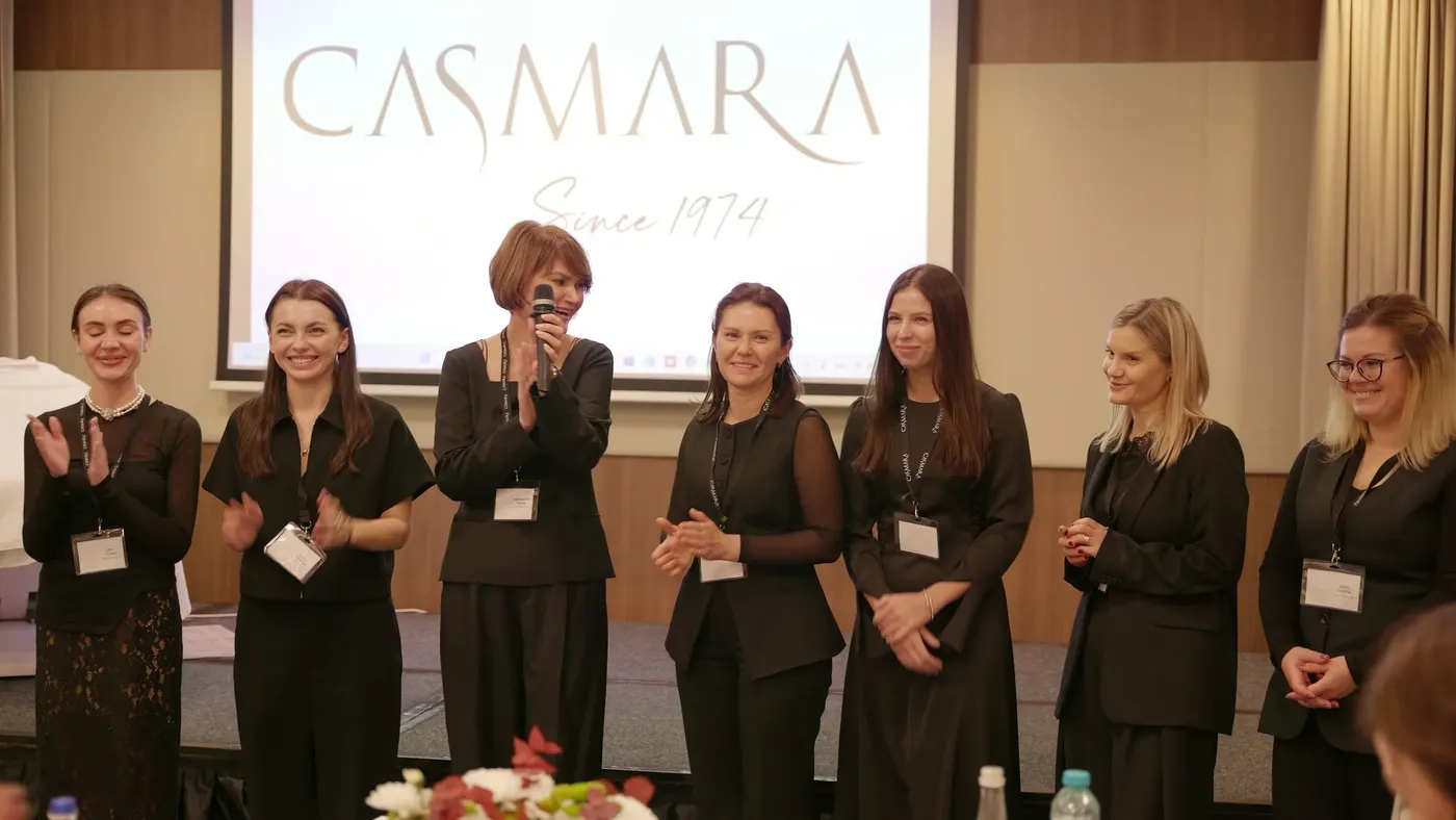 Echipa Casmara aplaudă pe scena seminarului, iar prezentatoarea vorbește la microfon; pe ecran, sigla Casmara