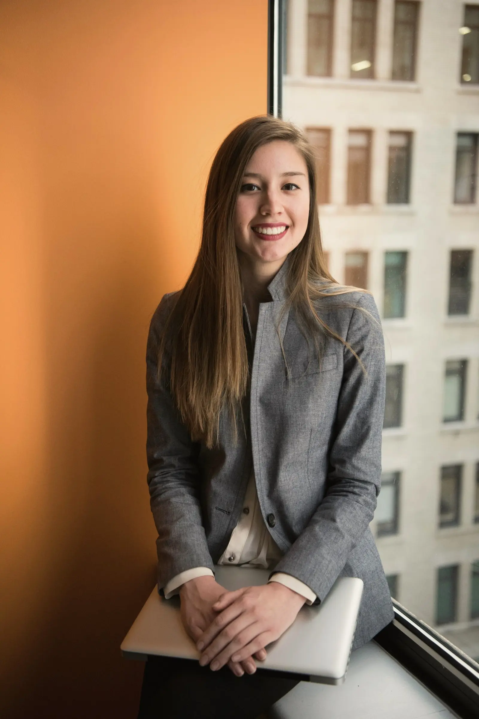 Businesswoman in a grey blazer smiling by a window