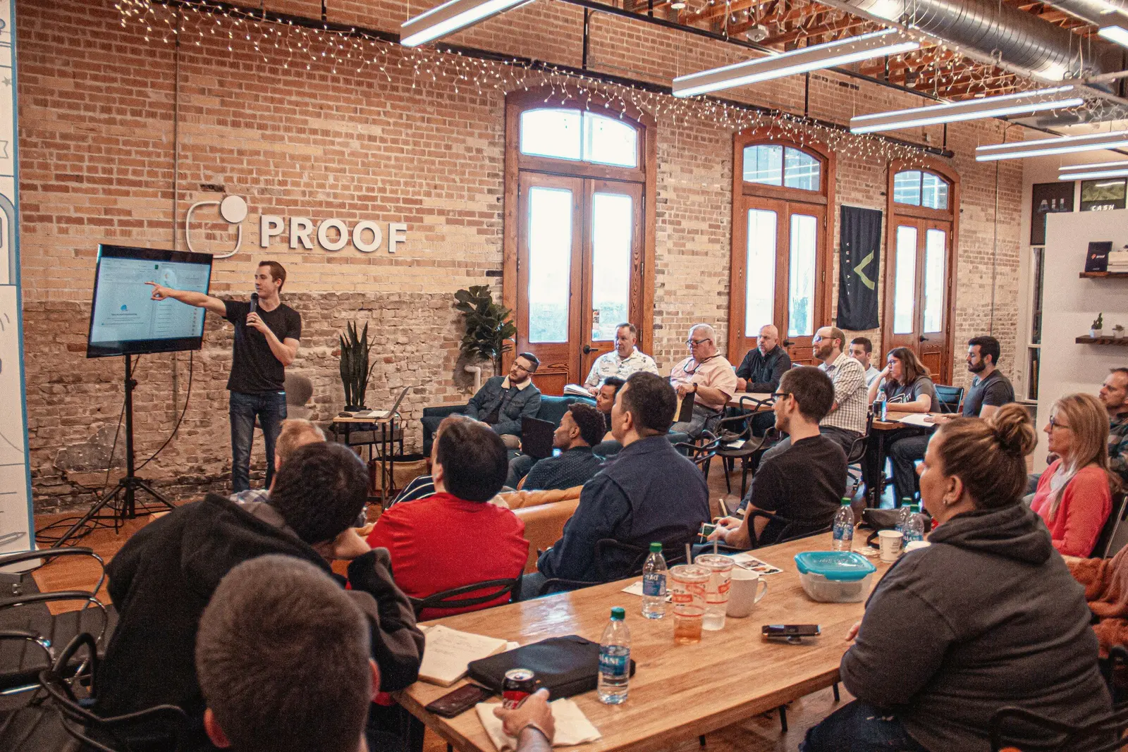 Speaker presenting to a seated audience in a brick-walled hall